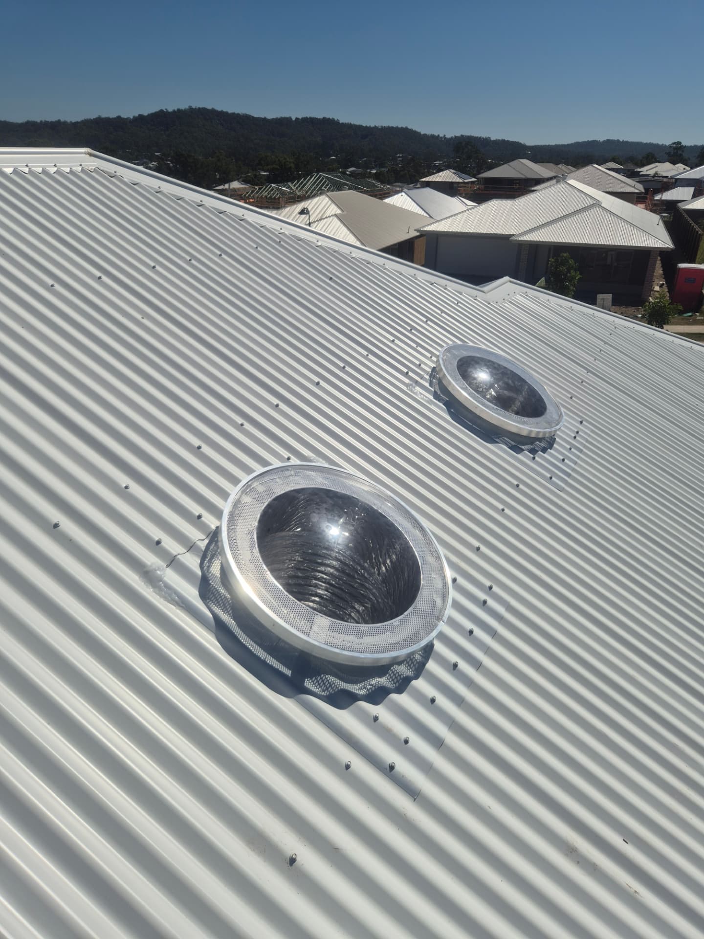 Two round dome skylights installed on a white corrugated metal roof